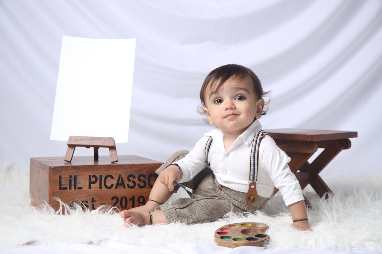 Adorable baby posing with paint palette in an art-themed studio setup.